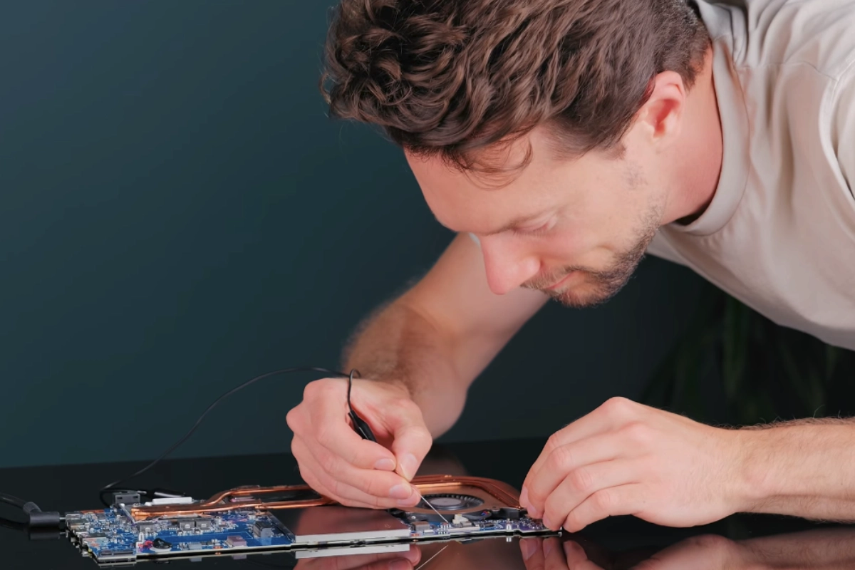 Matt probing the keyboard connector of a bare laptop motherboard with a multimeter