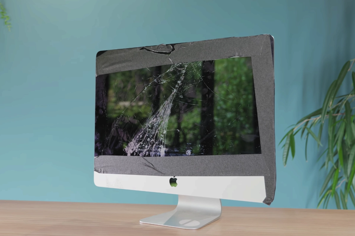 A smashed iMac with its cracked screen taped over, standing on a wooden desk