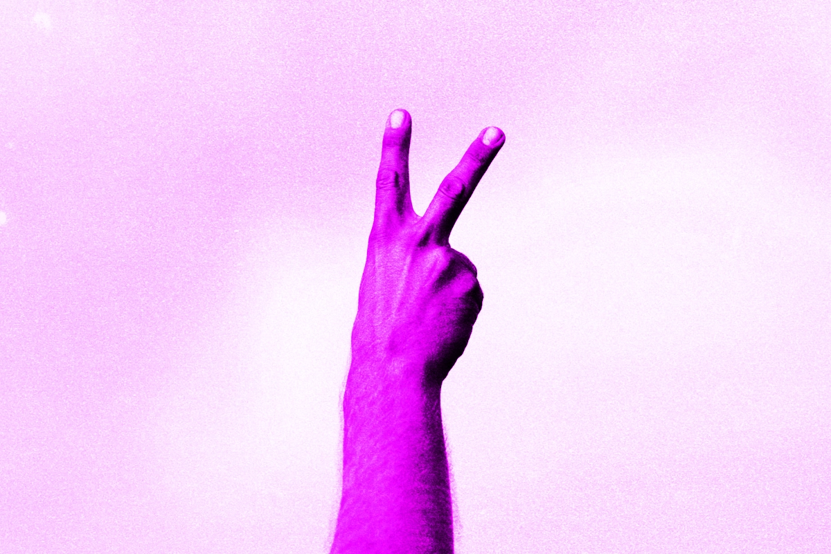 A raised hand making a peace sign, tinted bright magenta against a pale pink background