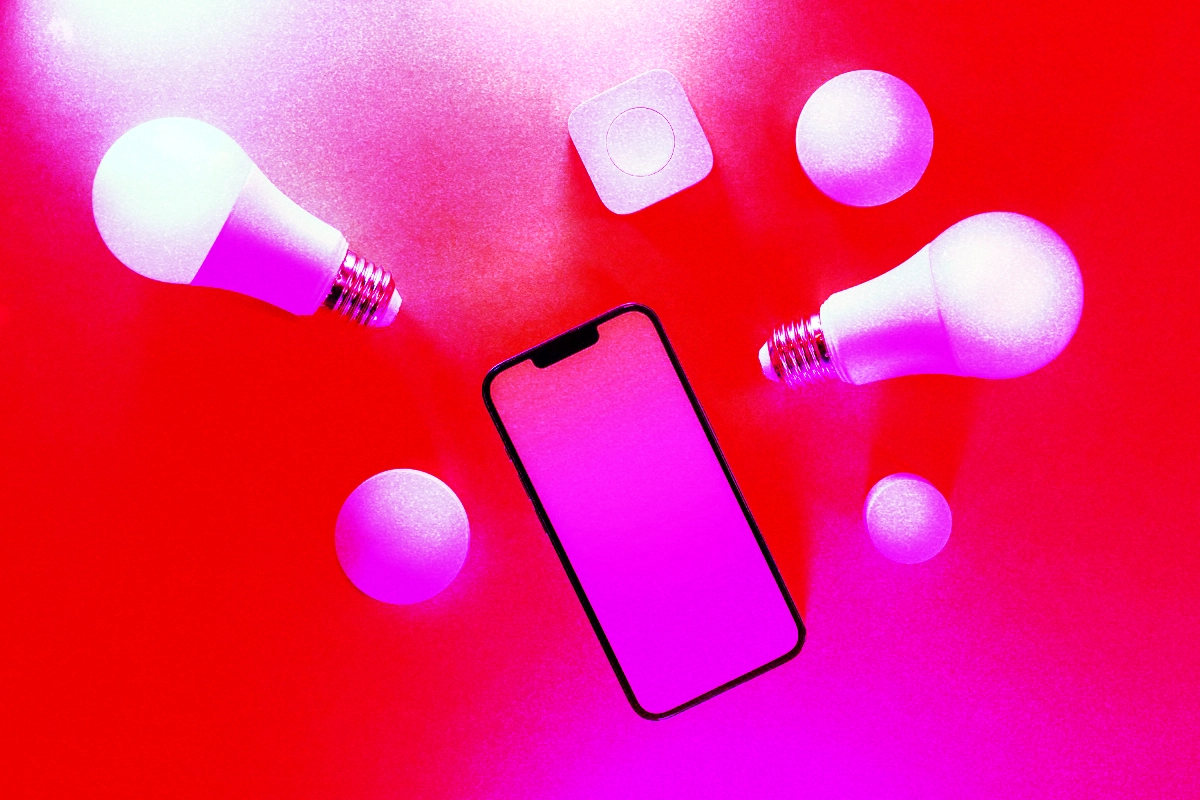 Smartphone lying among smart bulbs and a small hub button on a bright red surface