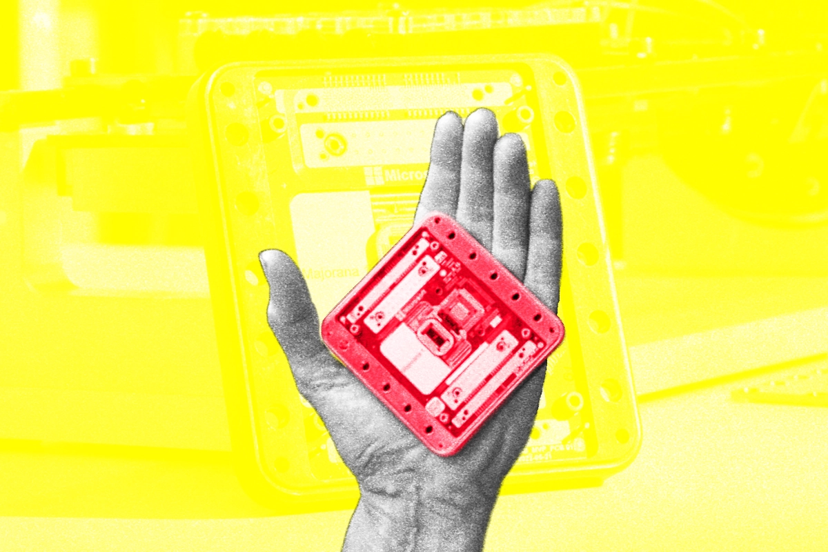 A grayscale hand holds a small red tinted quantum chip against a yellow lab background