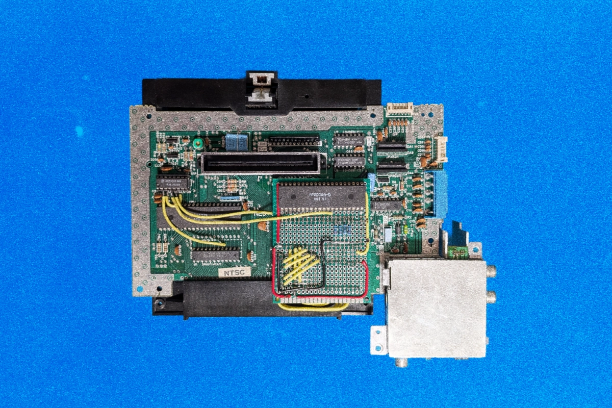 Opened NES console board with a hand-soldered prototype daughterboard and yellow jumper wires on blue