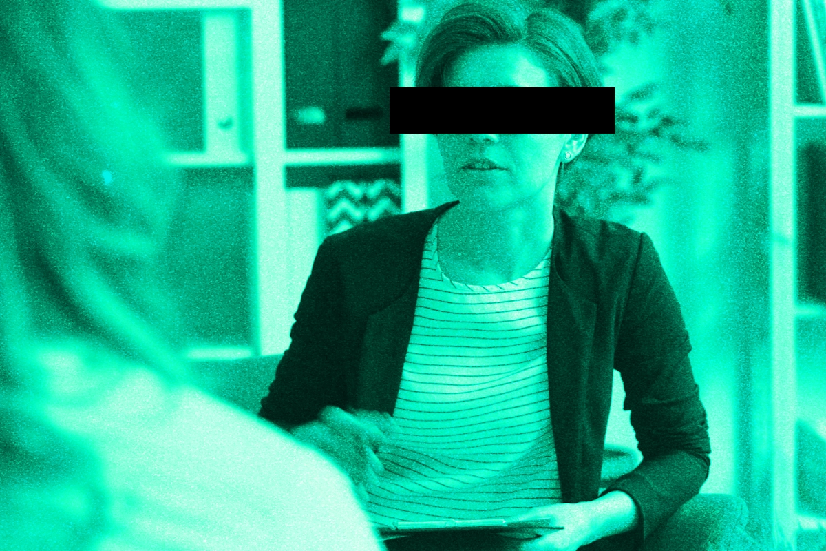 Green-tinted photo of a woman in a blazer with a black bar censoring her eyes during a meeting