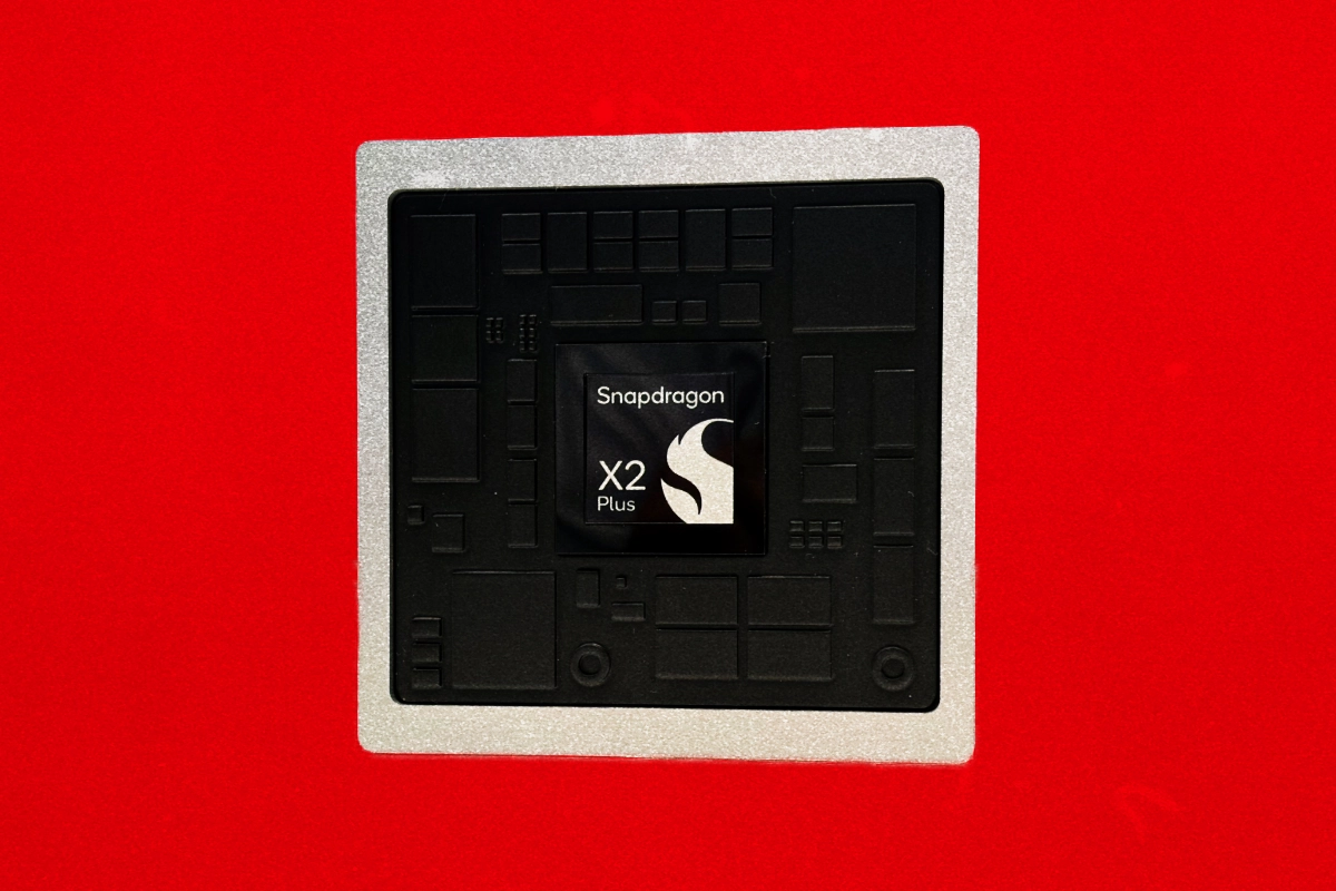 Black processor chip labeled "Snapdragon X2 Plus" on a silver package against a red background