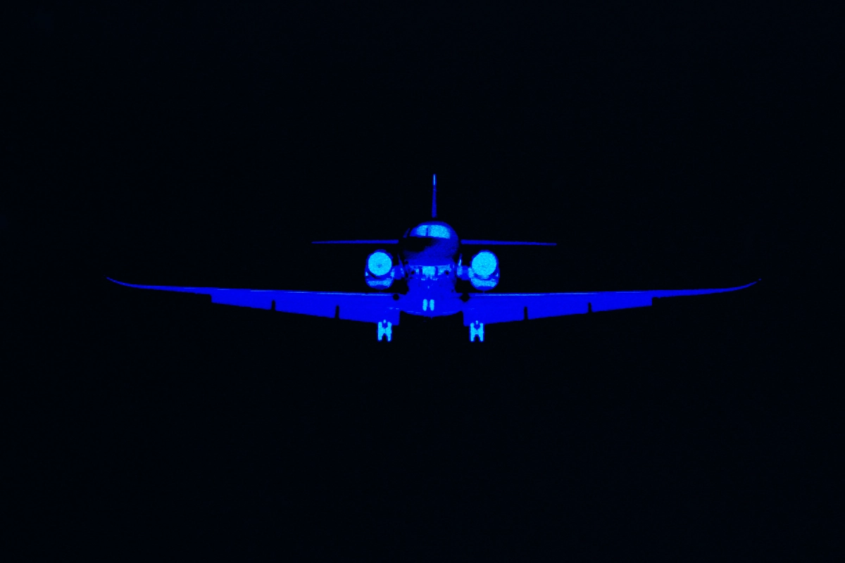 Blue-tinted silhouette of a private jet flying head-on against a black sky