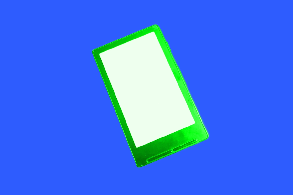 A small pocket e-ink reader with a 4.3 inch screen showing a book page, lying next to a USB-C cable